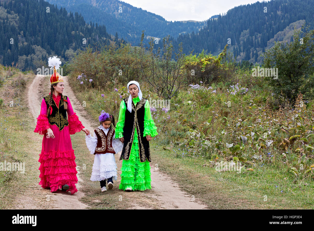 Kasachische Frauen in Nationalkostümen und ein Mädchen, das in der Natur in Almaty, Kasachstan, spazierengeht Stockfoto