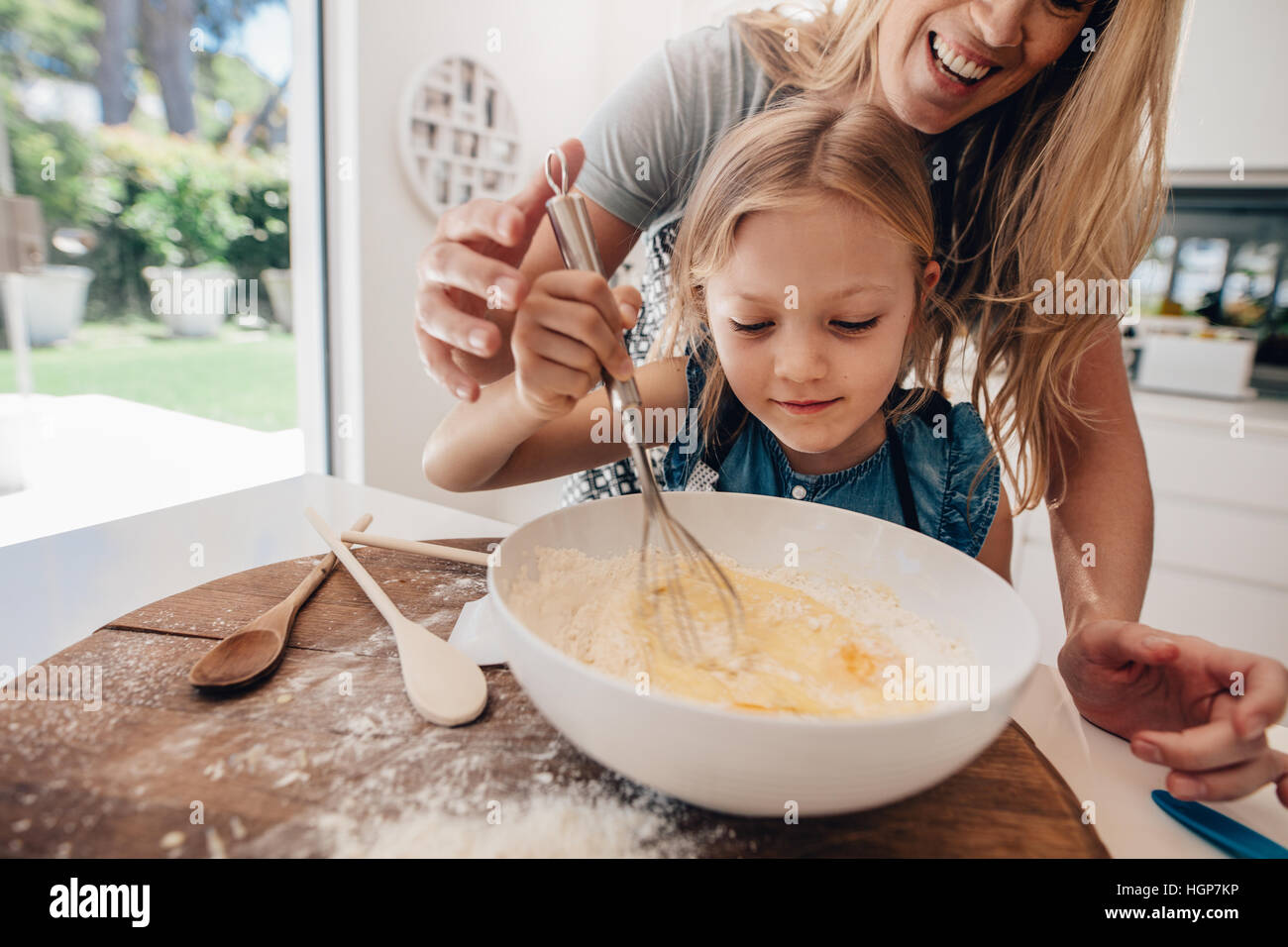 Fröhliches junges Mädchen mit ihrer Mutter, der Teig in der Schüssel mischen. Mutter und Tochter schlagen Teig in Küche. Stockfoto