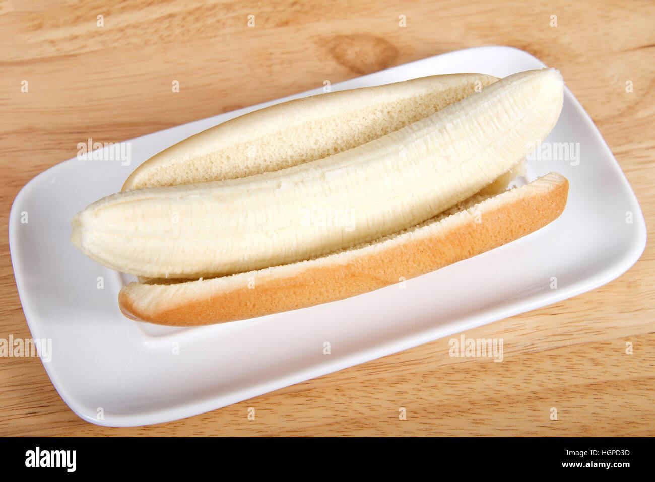 Banane in einem Hot-Dog-Brötchen serviert auf einem weißen rechteckigen Teller serviert auf einem Holztisch. Ansicht von oben aus einem Winkel Stockfoto