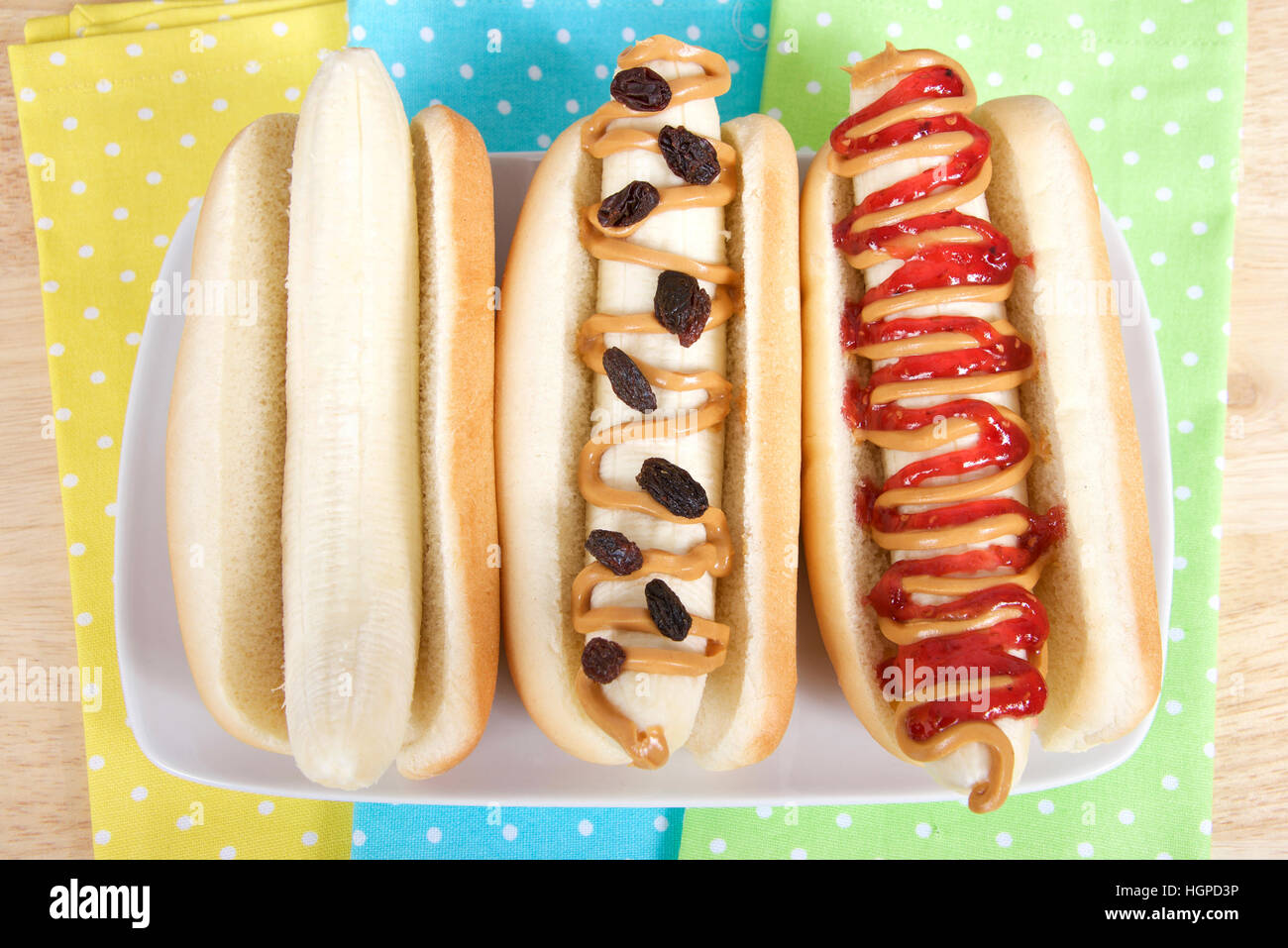Bananen-Hund-Sandwiches auf einer rechteckigen Platte mit gelben, grünen und blauen Tupfen Servietten unter. Banane in einem Hot-Dog-Brötchen, schlicht, mit Erdnuss, aber Stockfoto