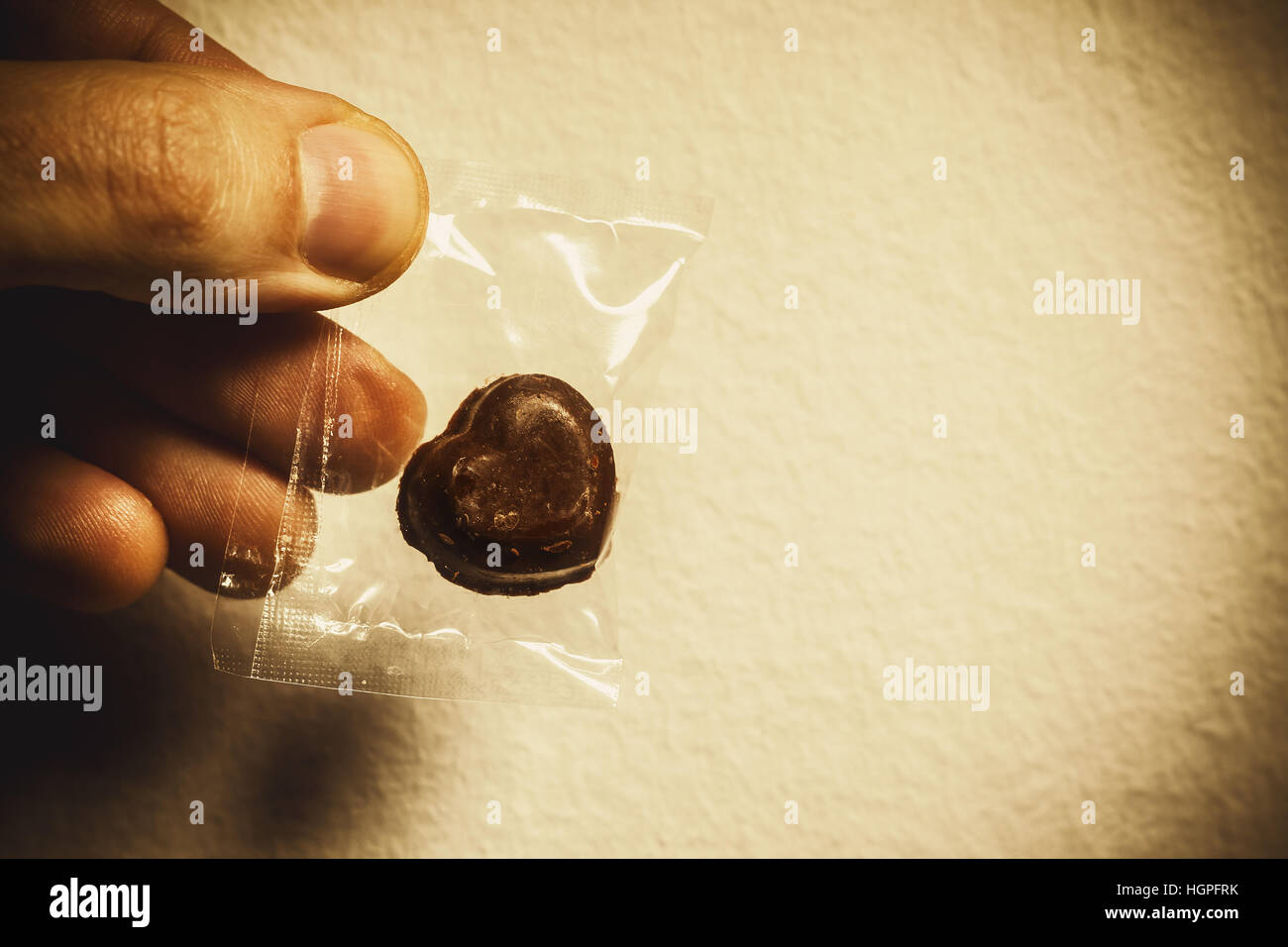 Schokoladenherz gewickelt in Plastiktüte, in der männliche Hand, konzeptuelle Komposition über Liebe geben. Stockfoto