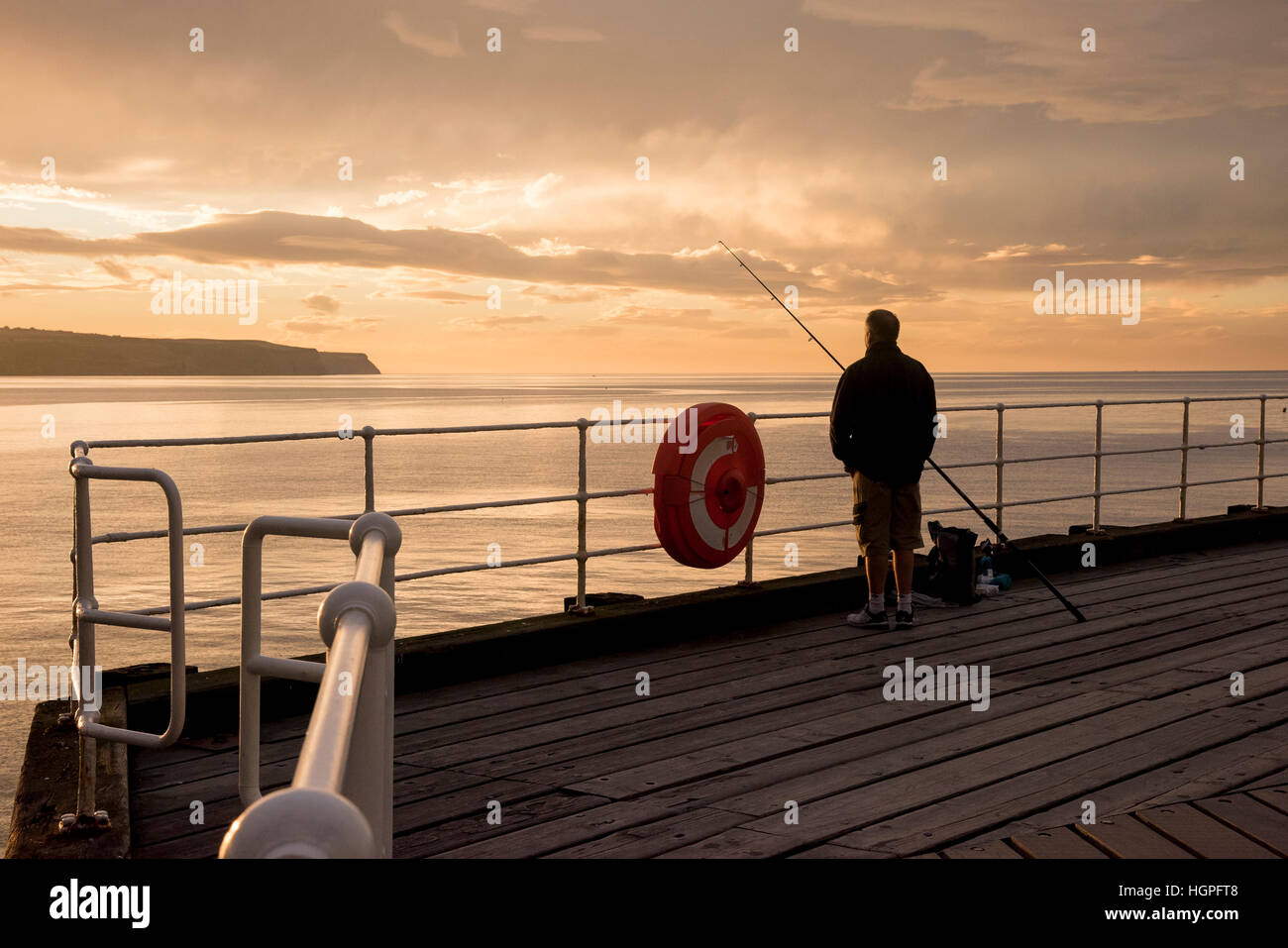 Malerische Whitby & gegen die drastischen, farbenfrohen sonnenuntergang himmel Silhouette, Mann (Angler) ist der Seefischerei von West Pier - North Yorkshire, England, UK. Stockfoto