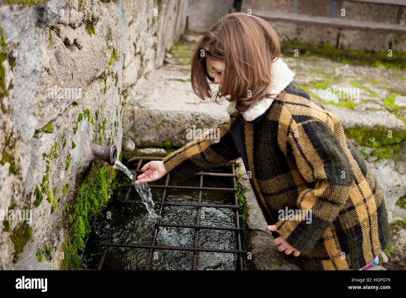 Kleine Mädchen berühren Wasser aus einem natürlichen Brunnen Stockfoto