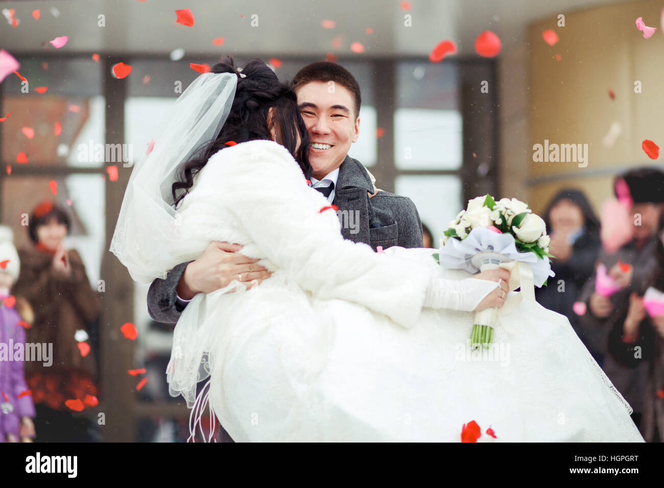 Der Bräutigam die Braut in seinen Armen, wirft das Publikum Blütenblätter und Reis. Glückliche Hochzeit. Stockfoto