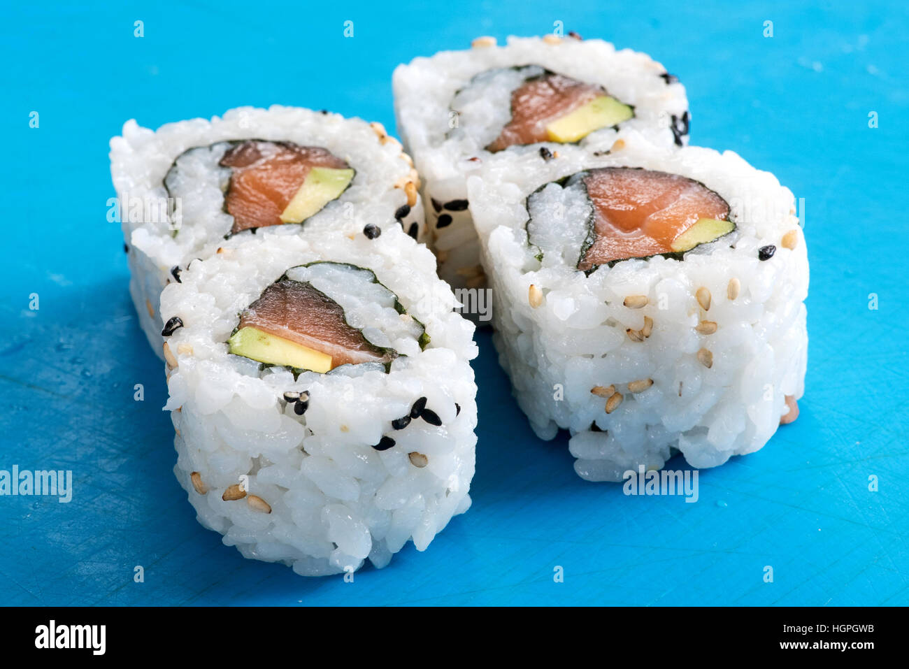 Vier frisch zubereitete rohen Lachs und Avocado Urumaki Sushi-Rollen in einer Nahaufnahme auf blauem Grund konzeptionelle des japanischen Fischküche Stockfoto