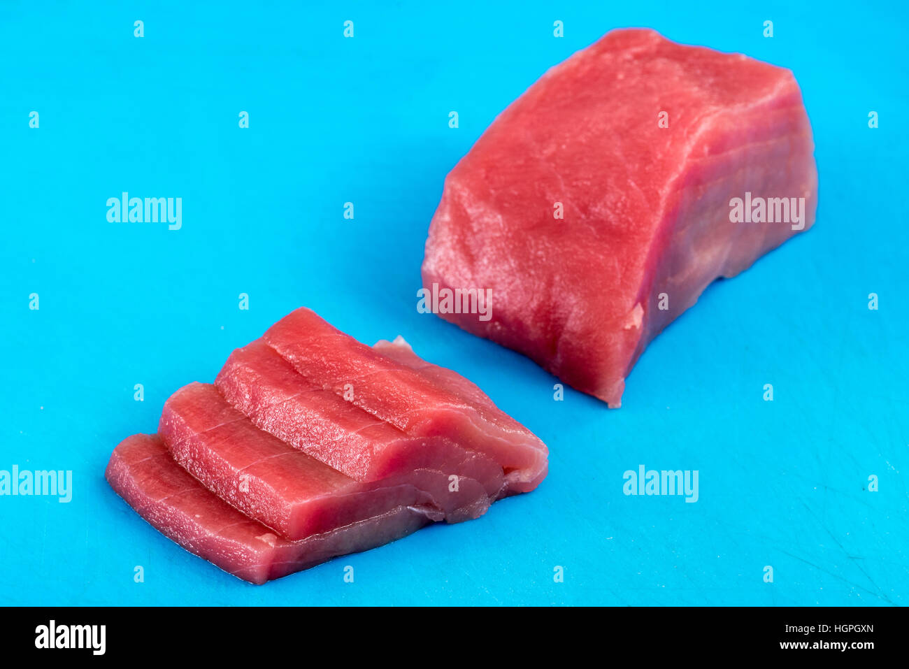 In Scheiben geschnittenen frischen rohen Thunfisch Filet oder Steak für den Einsatz in japanische Sushi und Sashimi, die diagonal angeordnet auf einem blauen Hintergrund mit Textfreiraum Stockfoto
