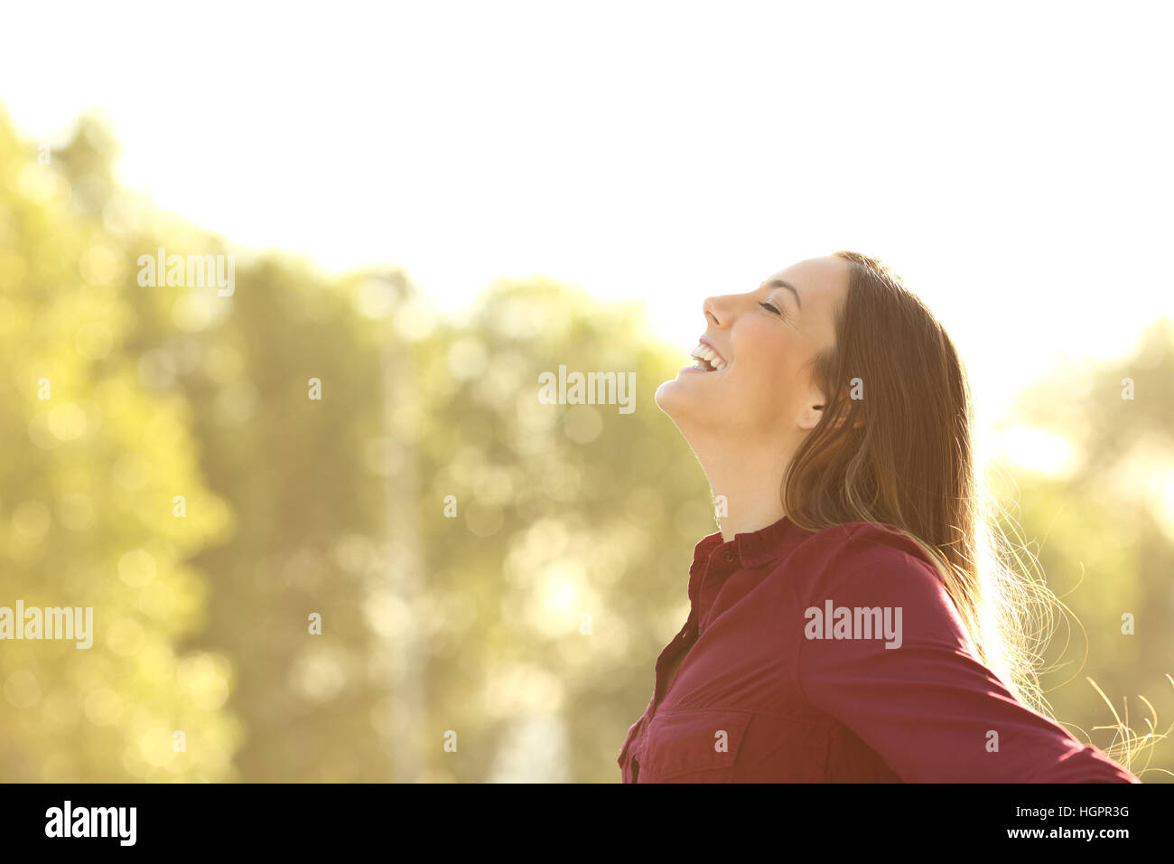 Seitenansicht der eine glückliche Frau, die frische Luft im Freien mit einem grünen Hintergrund und ein warmes Licht Stockfoto