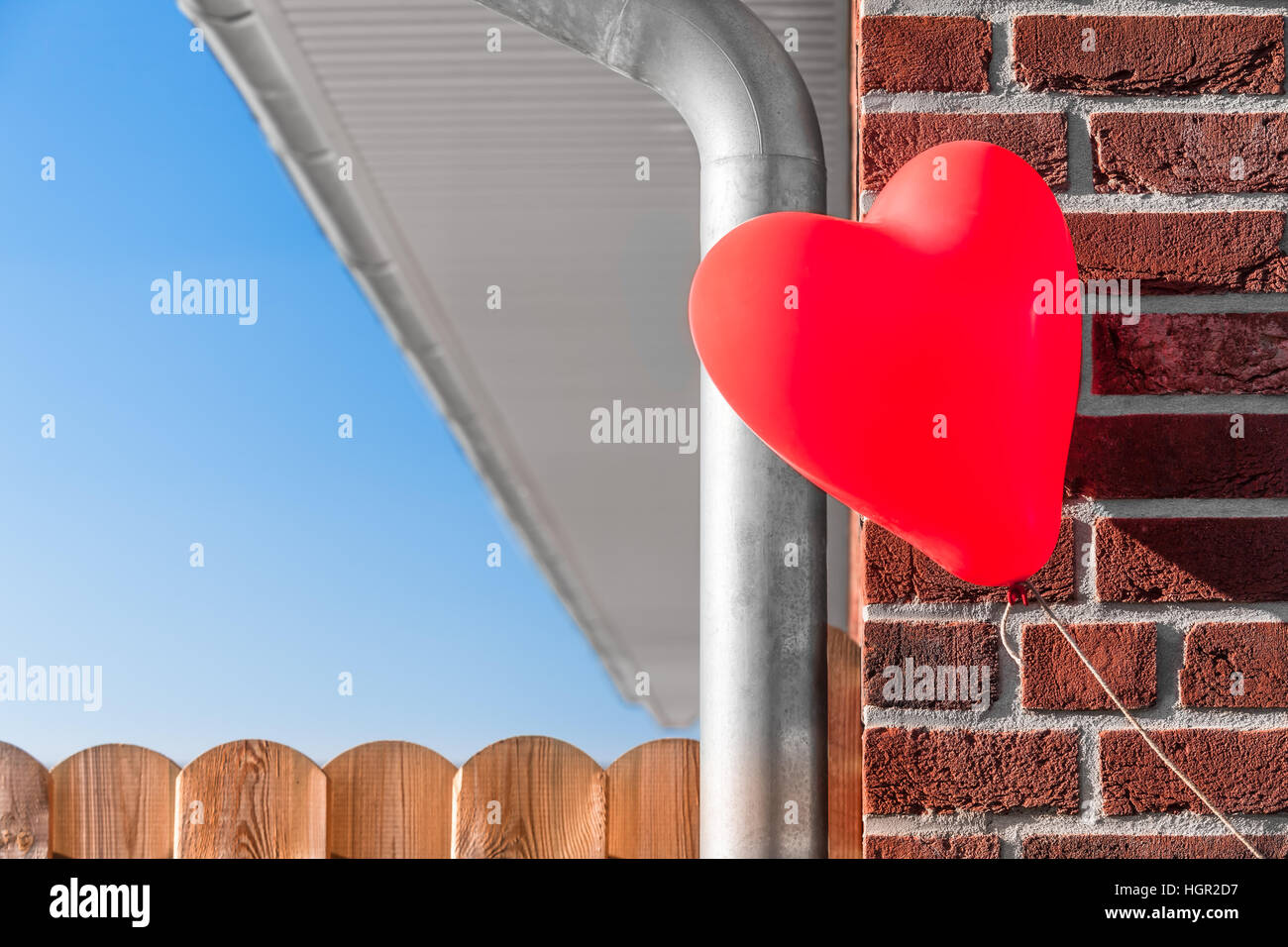 Teil von Backstein Haus mit Wasser Abflussrohr bauen, Zaun, schwimmende roten herzförmigen Ballon am Ecke - Traum Haus zu besitzen an Bord Stockfoto