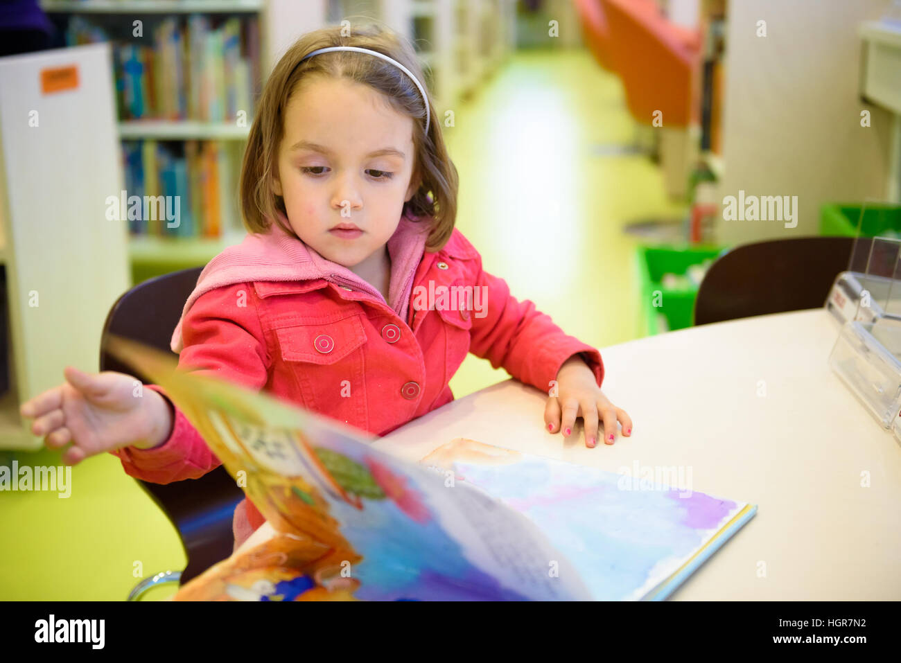 Kleines Mädchen ist ein Buch in der Bibliothek stöbern. Ein Kind sucht sich die Bücher in der Bibliothek entscheiden, welche man mit nach Hause nehmen. Kreativität der Kinder und Stockfoto