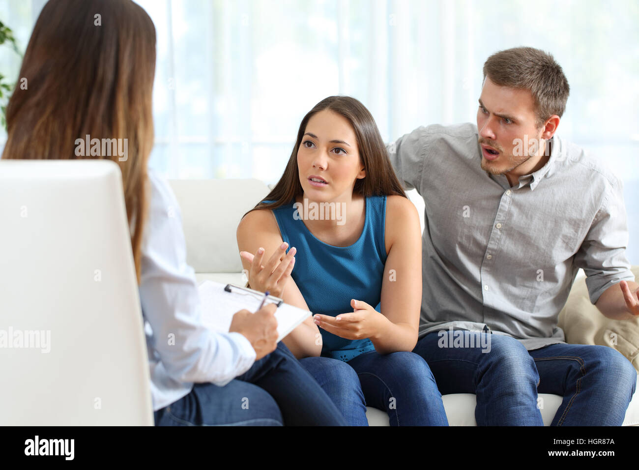 Wütend paar im Gespräch mit einem Eheberater während der Therapie auf einem Sofa im Wohnzimmer eines Hauses Stockfoto