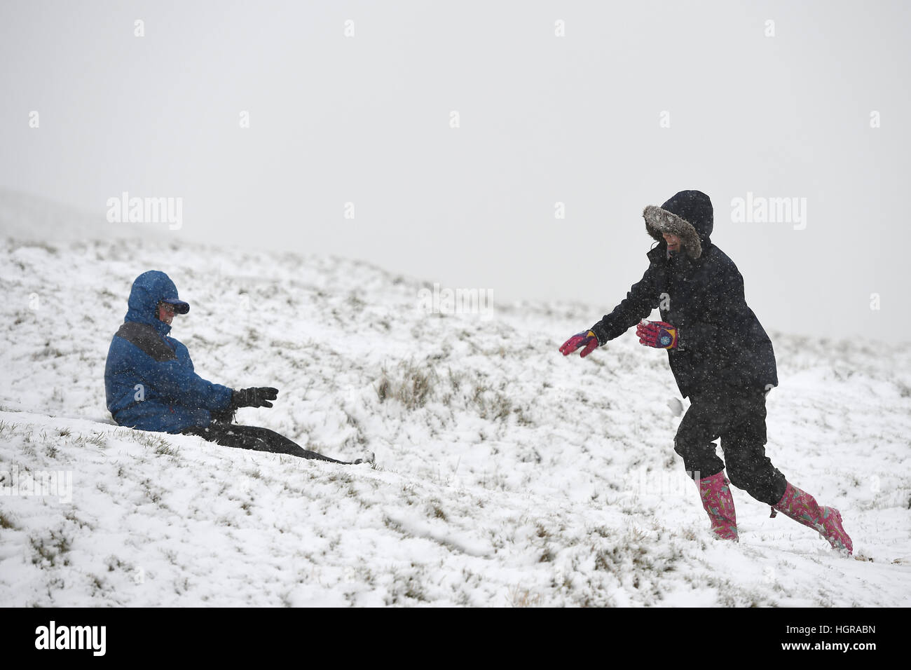 Terry Burrell (links) und seine Enkelin Elanor Rowbotham spielen im Schnee auf dem Mam Tor Hill im Peak District, während die Schneestürmbedingungen ansetzen und ganz Großbritannien einen echten Wintergeschmack geben wird. Stockfoto