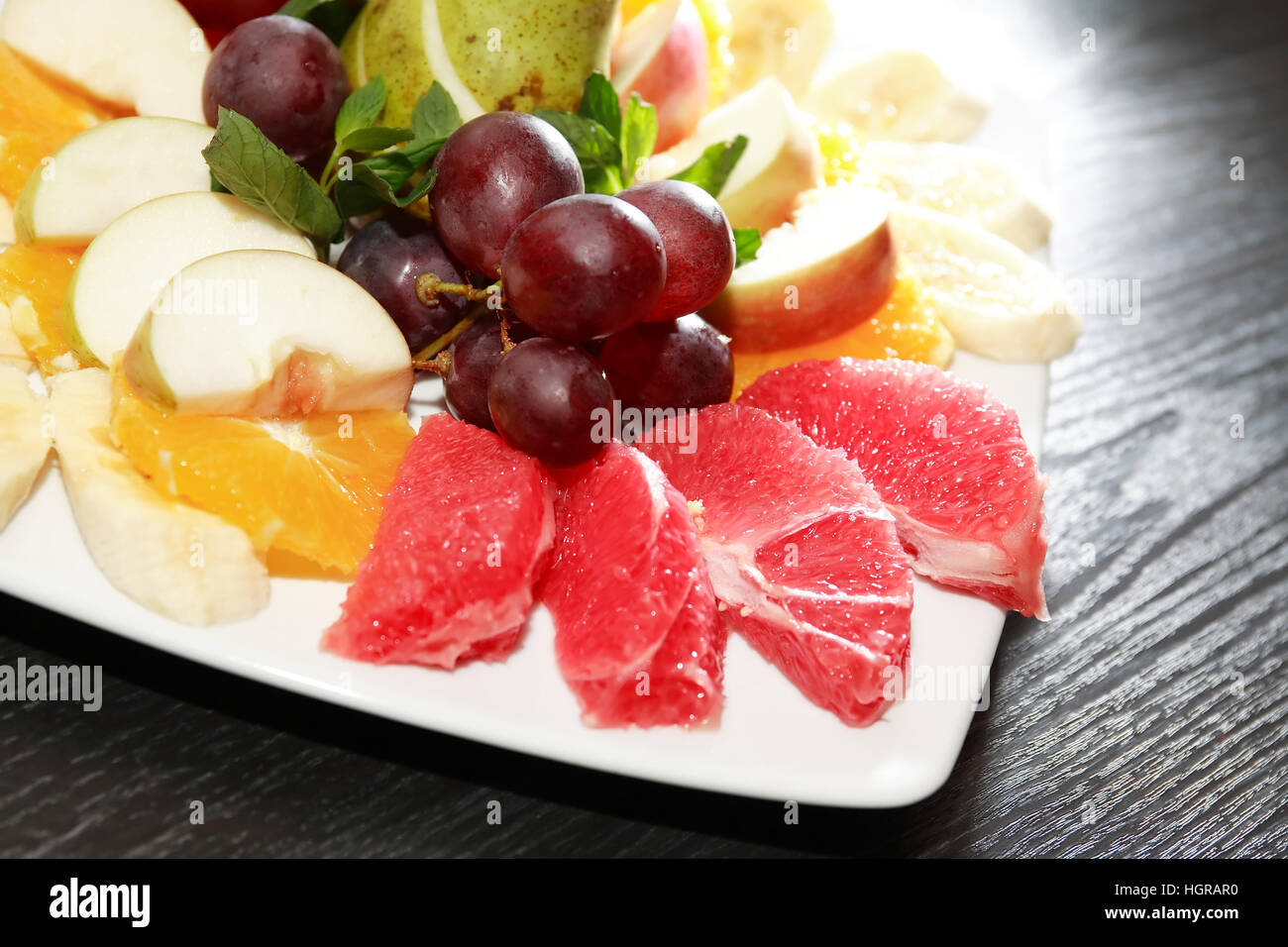 Platte mit verschiedenen geschnittenen Früchten auf dunklen Holztisch Stockfoto