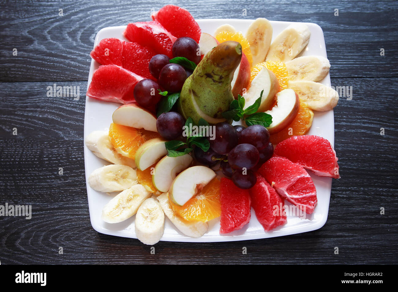 Platte mit verschiedenen geschnittenen Früchten auf dunklen Holztisch Stockfoto