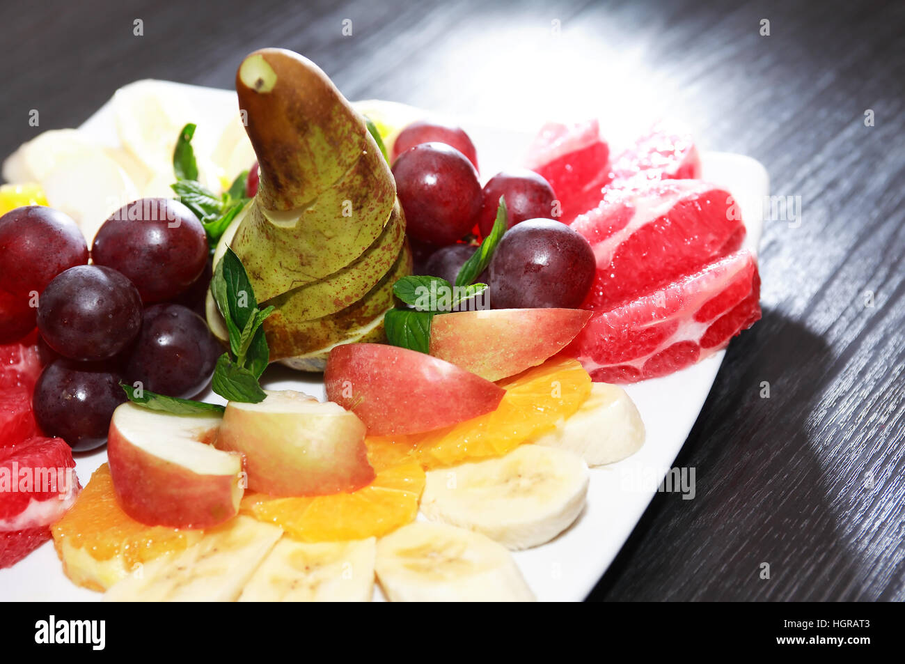 Platte mit verschiedenen geschnittenen Früchten auf dunklen Holztisch Stockfoto
