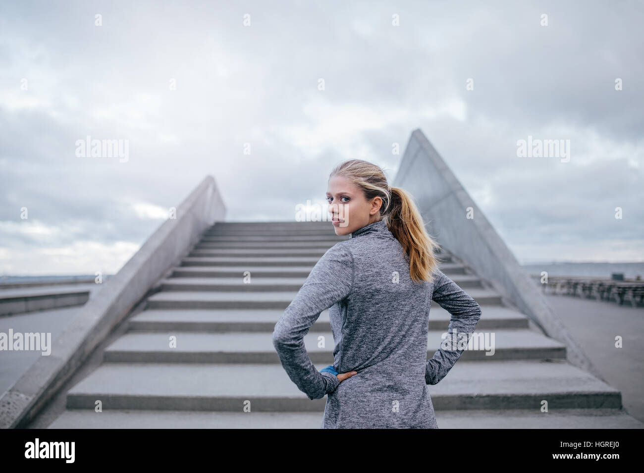 Außenaufnahme einer jungen Frau, die an einer Treppe steht und über die Schulter schaut. Fitnessmodell für Frauen bereit zum Laufen. Stockfoto