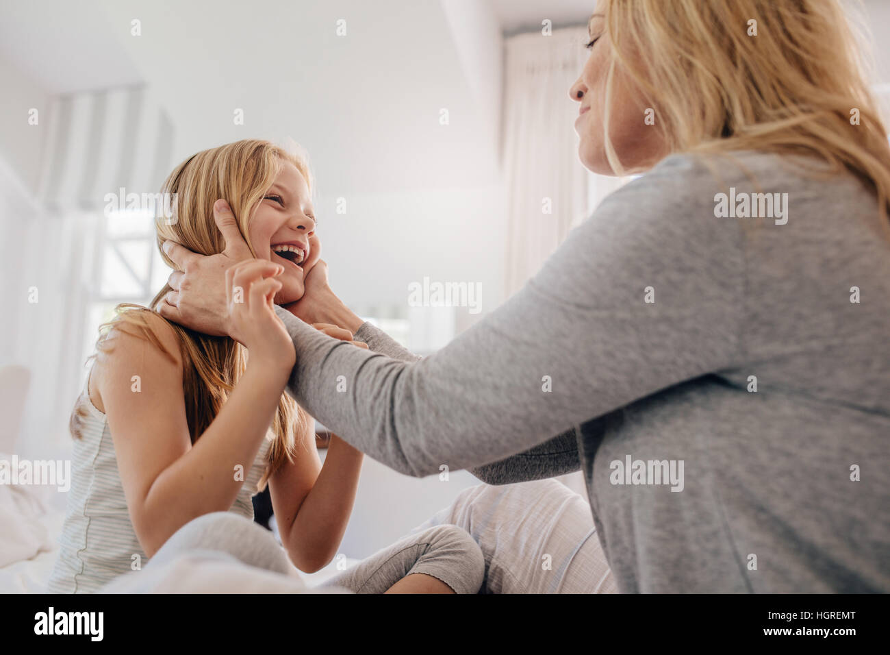 Frau mit Gesicht auf ihre niedliche kleine Mädchen. Liebevolle Mutter und Tochter am Bett sitzen und spielen. Stockfoto