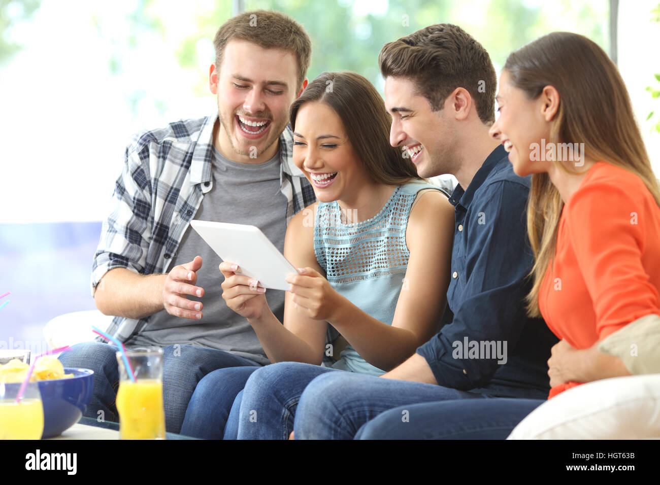 Vier lässig glücklich Freunde Lachen beobachten Medieninhalte zusammen in einer Tablette sitzen auf einem Sofa im Wohnzimmer zu Hause Stockfoto