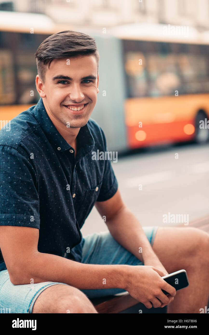 Lächelnder junge Mann sitzen auf einer Bank in der Stadt Stockfoto