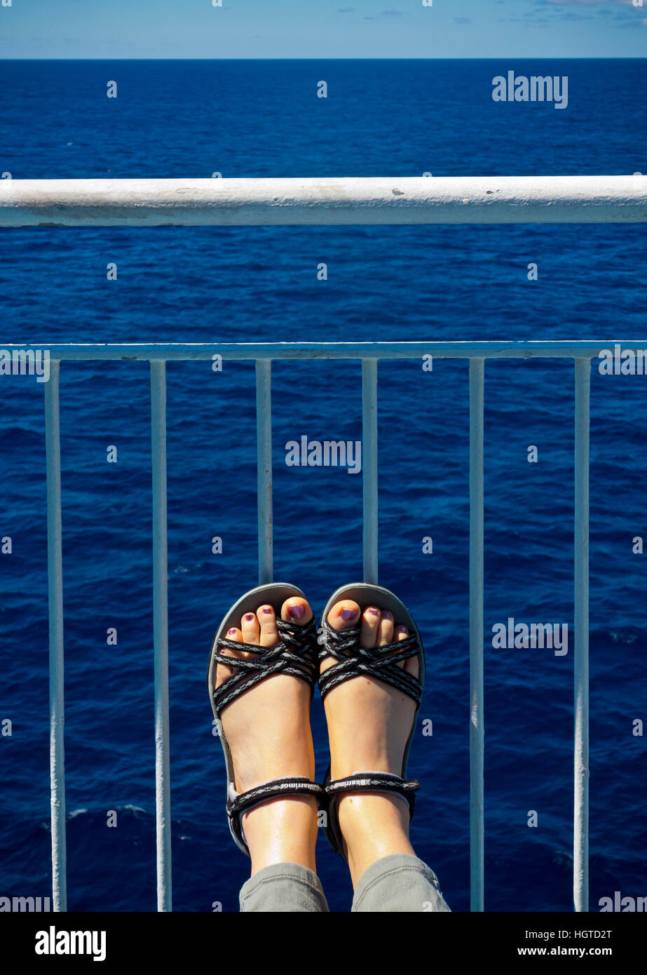 Frau auf dem Deck eines Schiffes mit ihre Füße gegen das Geländer auf einem ruhigen Sommertag mit blauem Himmel und Meer Stockfoto