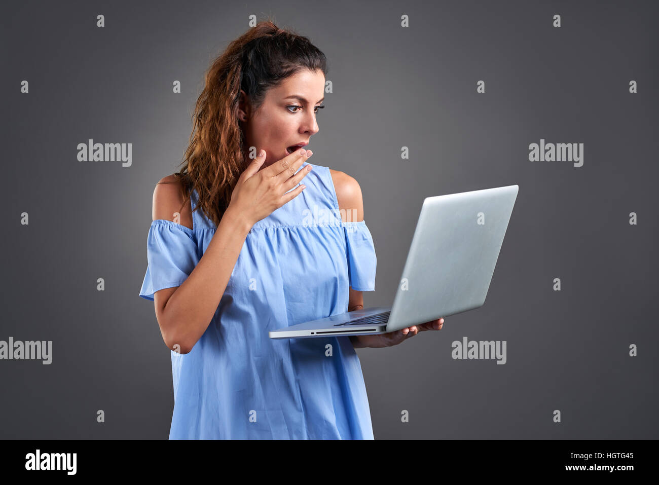 Eine schöne junge Frau stehend und Abholzung überrascht beim Betrachten eines Laptops in der Hand. Stockfoto