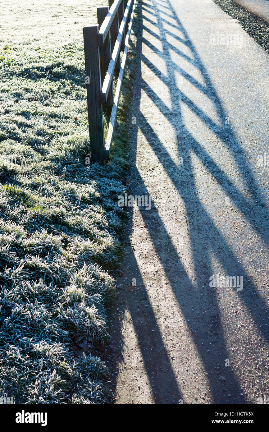 Eine Winterszene mit satiniertem Rasen und Zaun mit langen Winter Schatten Stockfoto