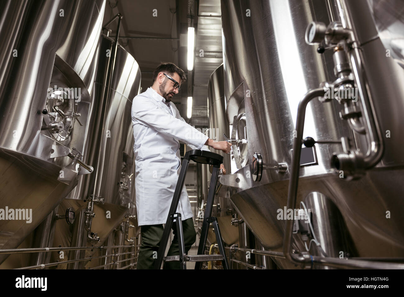 Ernster Mann mit Leiter und Brauen Mechanismus am Werk Stockfoto