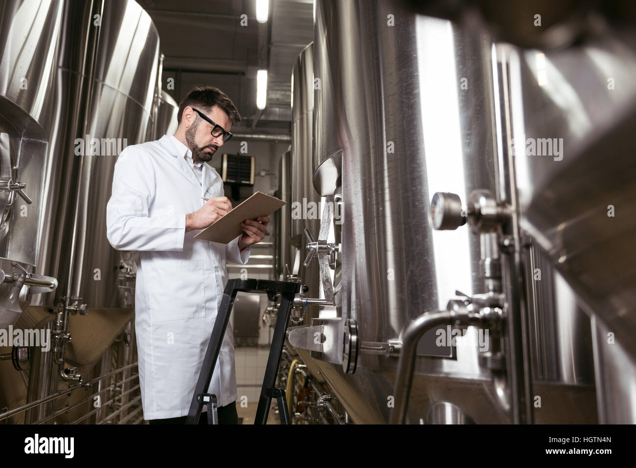 Erfreut Mann mit Leiter und Brauen Mechanismus am Werk Stockfoto