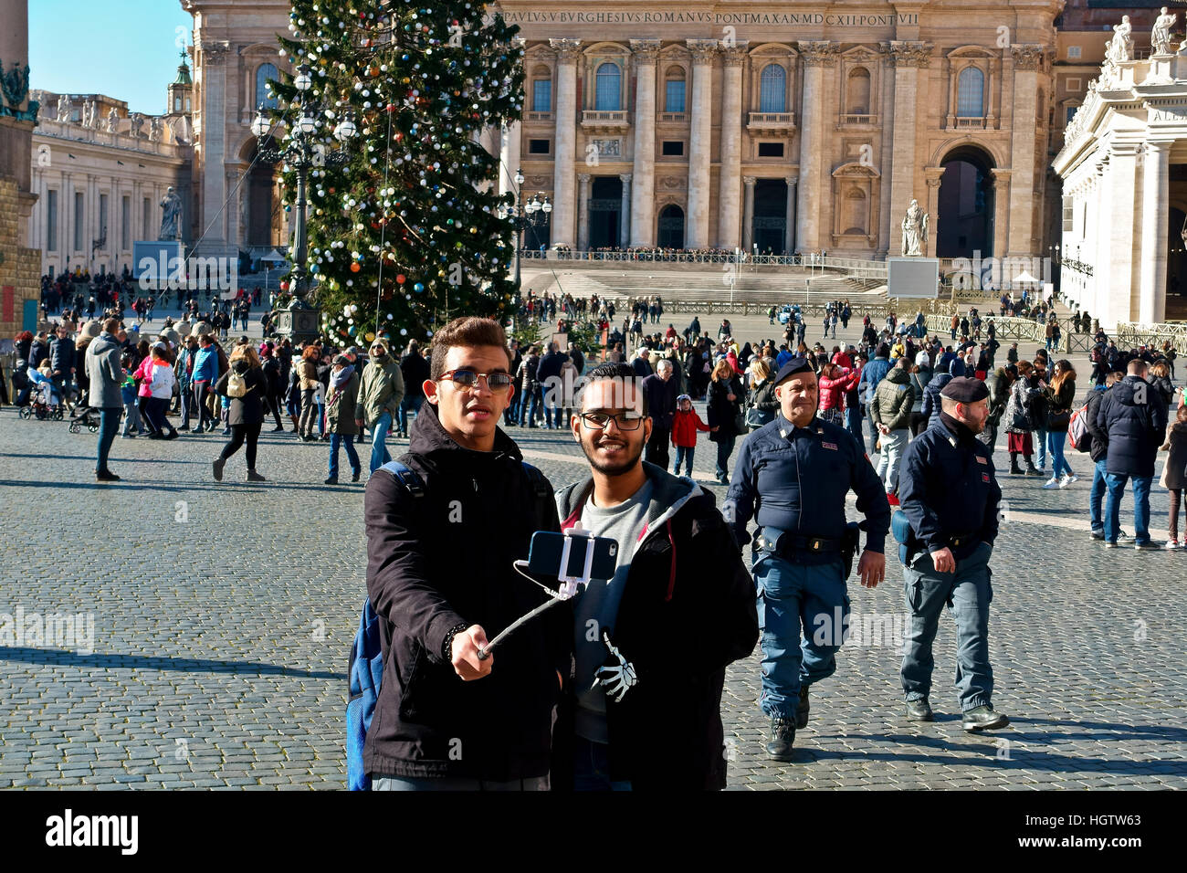 Zwei Freunde unter saelfie mit Smartphone mit Stick am Petersplatz (Piazza San Pietro) Vatikanstadt, auf einem Winter sonniger Tag. Rom Weihnachten Stockfoto
