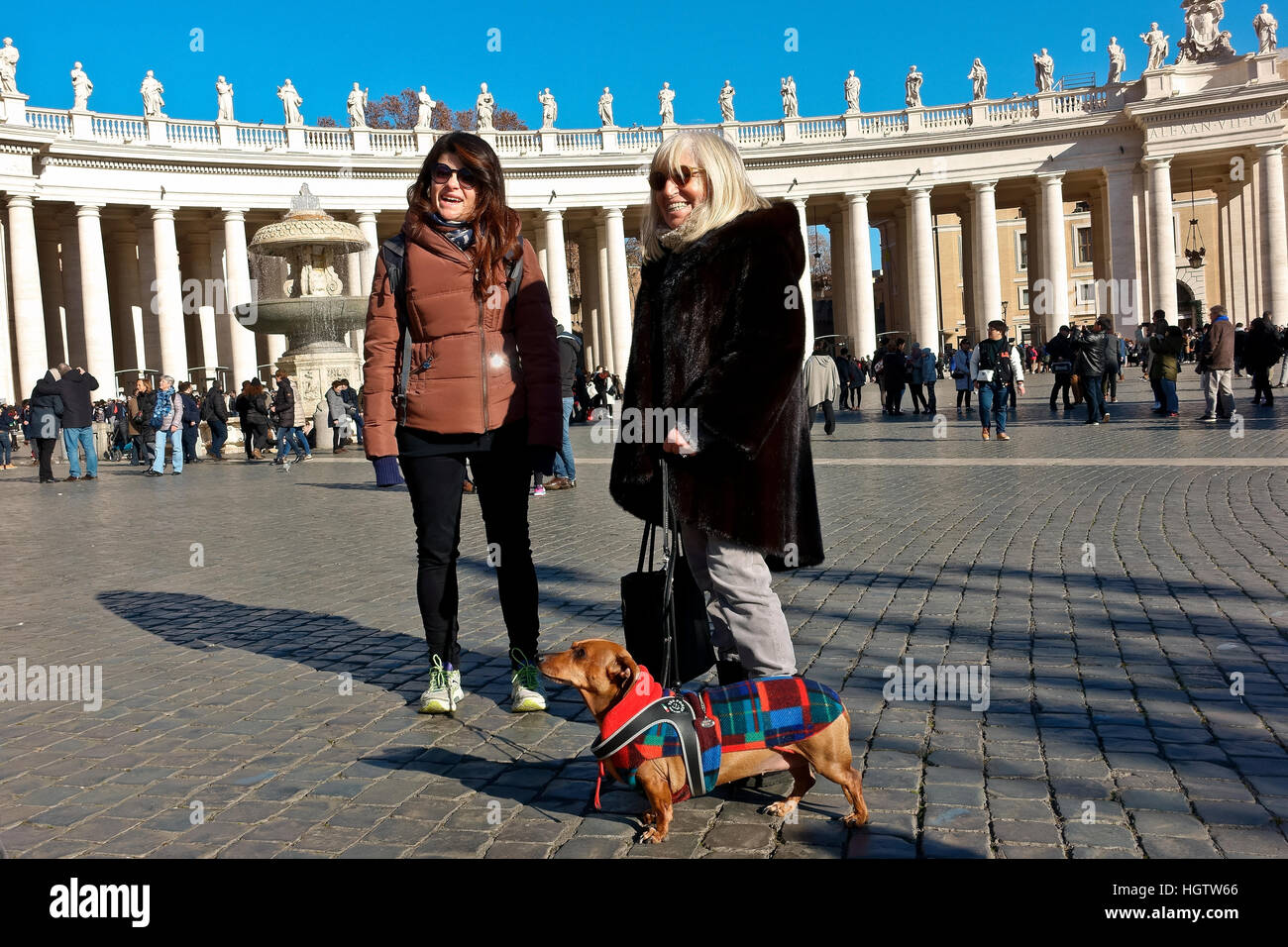 Mutter und Tochter stehen auf dem Petersplatz, während sie ihren Dackel-Hund an einem sonnigen Wintertag, blauem Himmel, spazieren gehen. Vatikan, Rom, Italien, Europa. Stockfoto