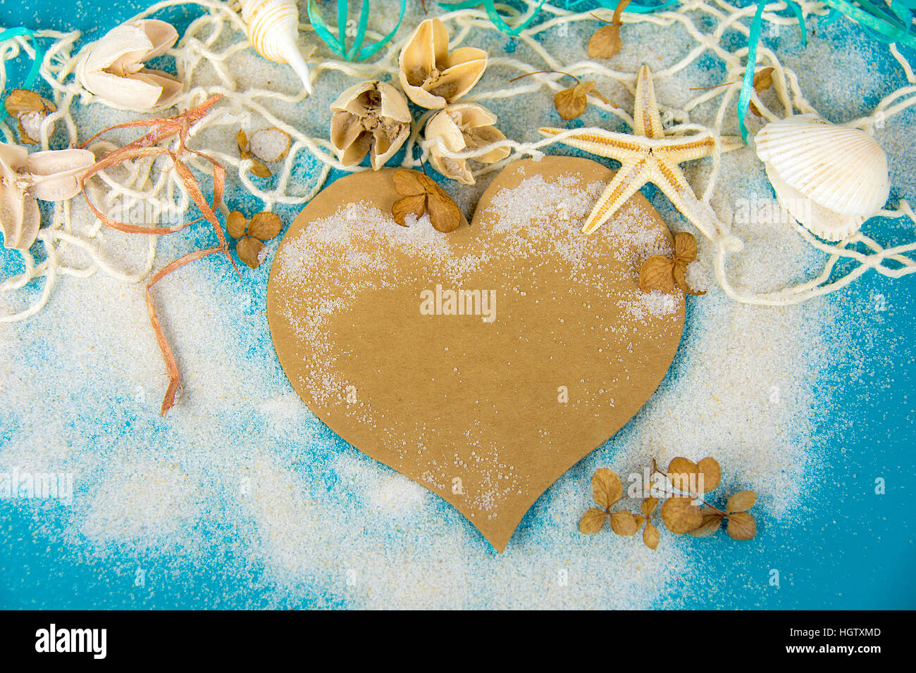 braune Herz und Muscheln im Netz und Sand auf Türkis lackiertem Holz Stockfoto