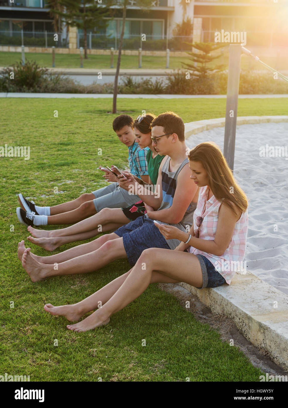 Gruppe von Jugendlichen mit ihren digitalen Geräten im Freien im Abendlicht. Konzept der drahtlosen Kommunikation und verlieren reales Stockfoto