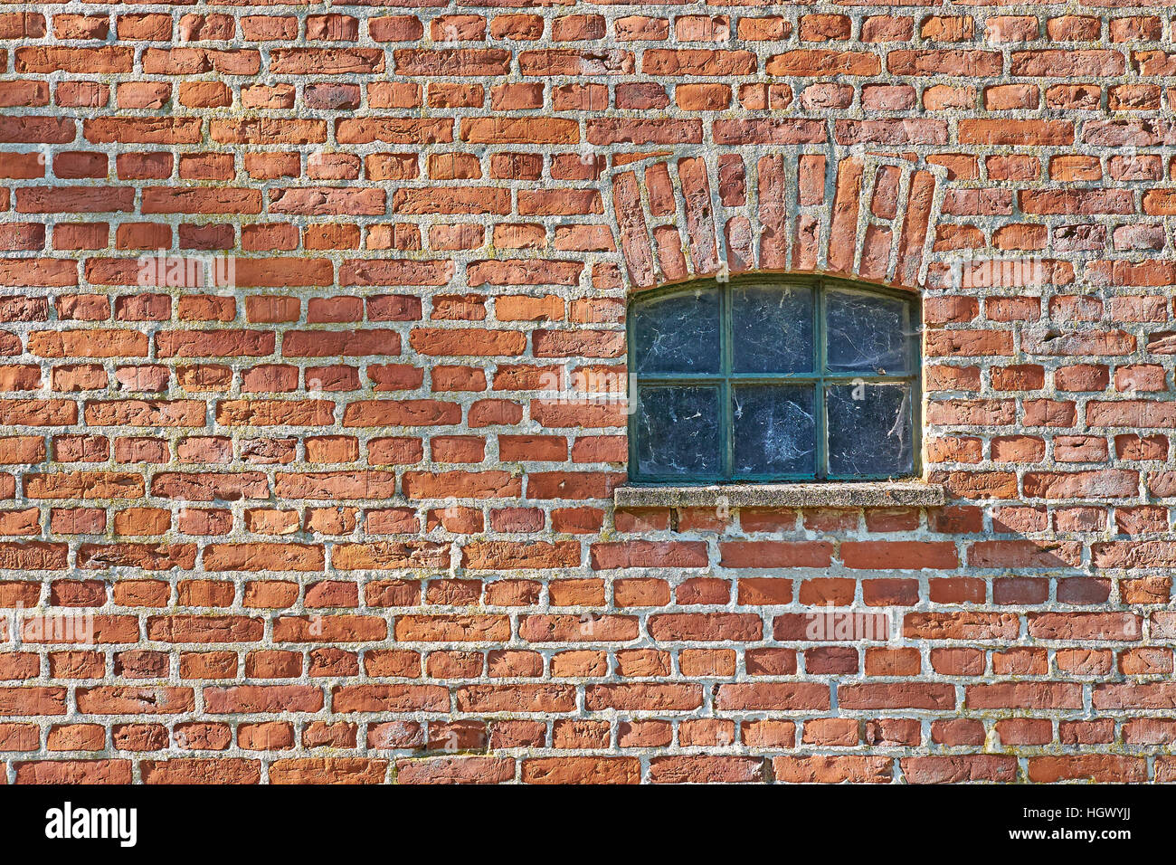 Kleine eiserne Scheune Fenster versenkt in einer roten Backsteinmauer. Spinnennetz in der Verglasung Stockfoto