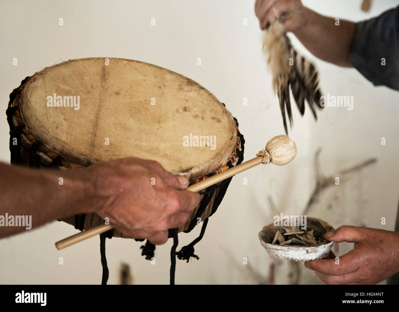 Schamanische Wisch Zeremonie mit Salbei, Federn und Trommel. Nahaufnahme von Händen mit den Attributen. Stockfoto