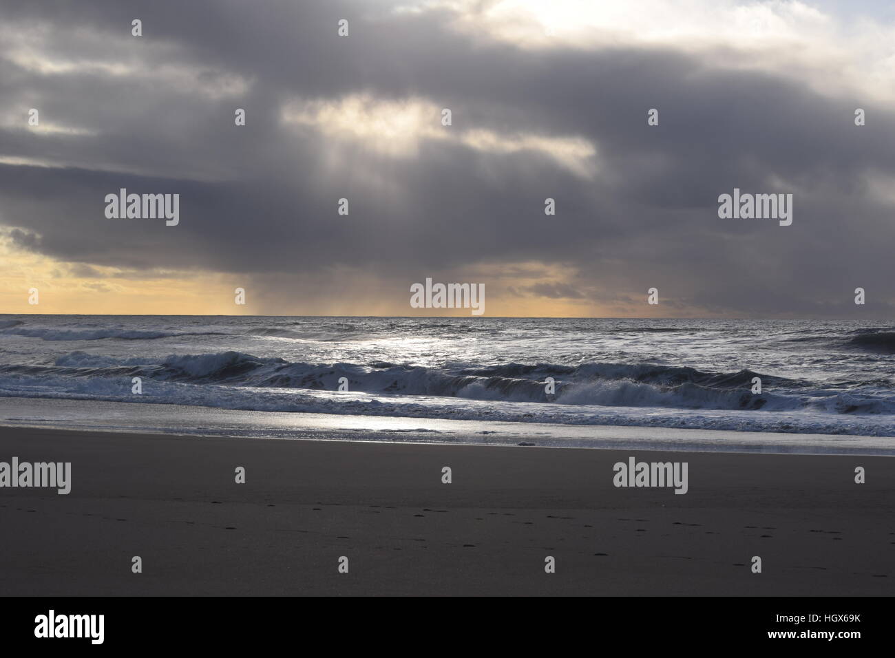 Sun peaks durch die dunklen Wolken und beleuchtet die Wellen Stockfoto