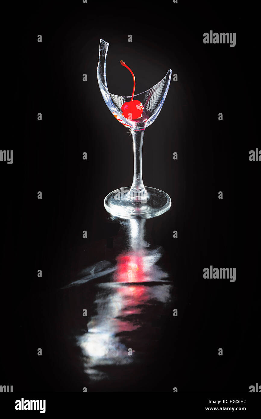 Zerbrochene Weinglas auf schwarzem Hintergrund mit Kirsche und Reflexionen.  Fotografiert im Studio auf reflektierende Matte. Stockfoto