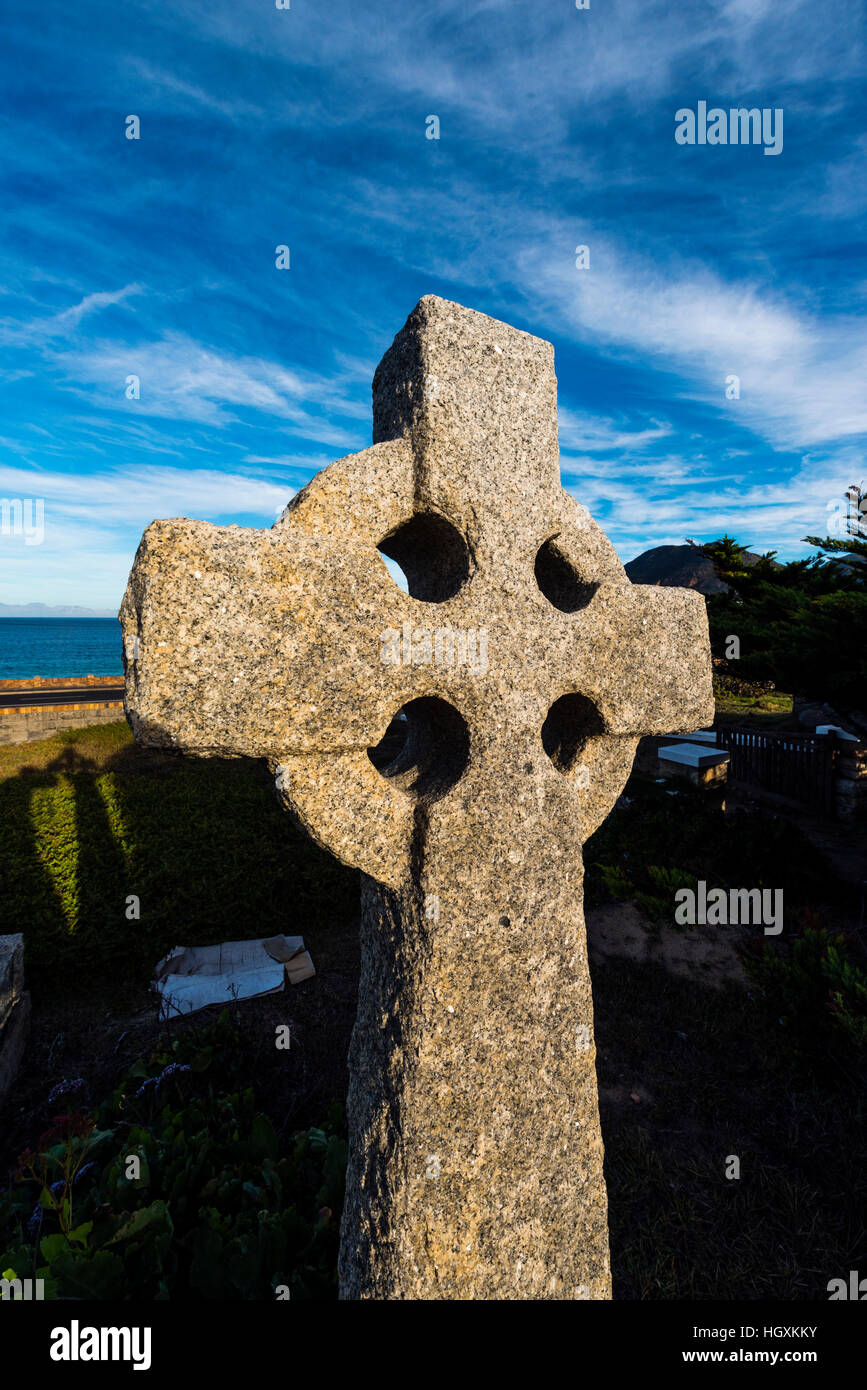 Ein Steinkreuz fängt das letzte Licht der untergehenden Sonne in einem küstennahen Friedhof. Stockfoto