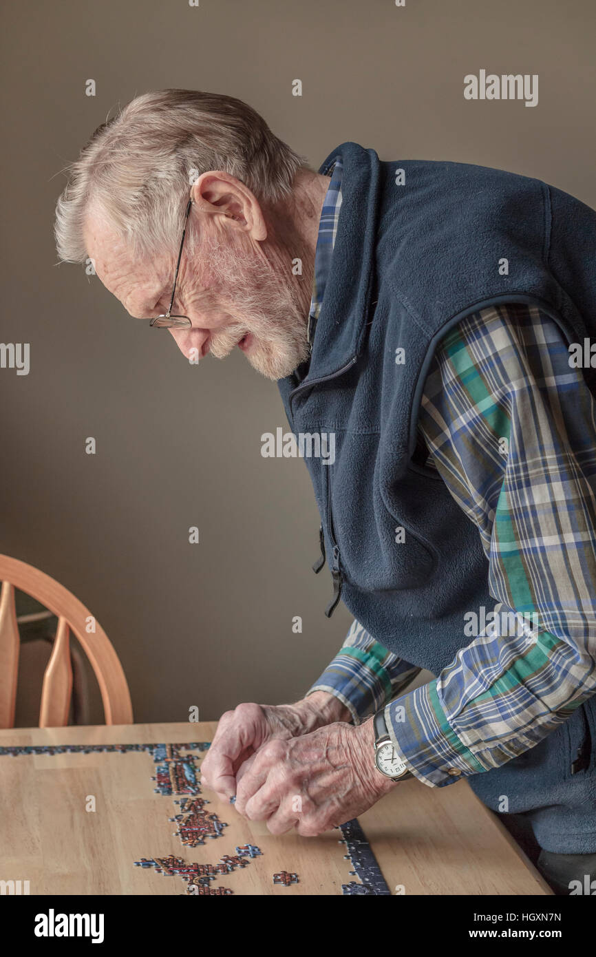 Eine ältere, bärtigen Mann (93 Jahre alt) das Tragen von Brillen und Hörgeräten arbeitet auf ein Puzzle in natürlichen Nachmittag Licht. Stockfoto