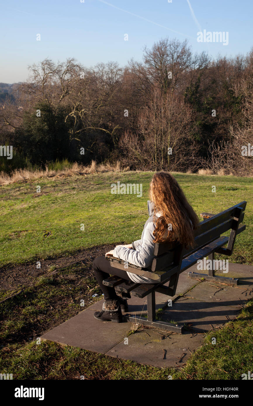 Junge Frau mit langen Haaren zurück zu Kamera, sitzen auf einer Parkbank, Blick in die Ferne. Stockfoto