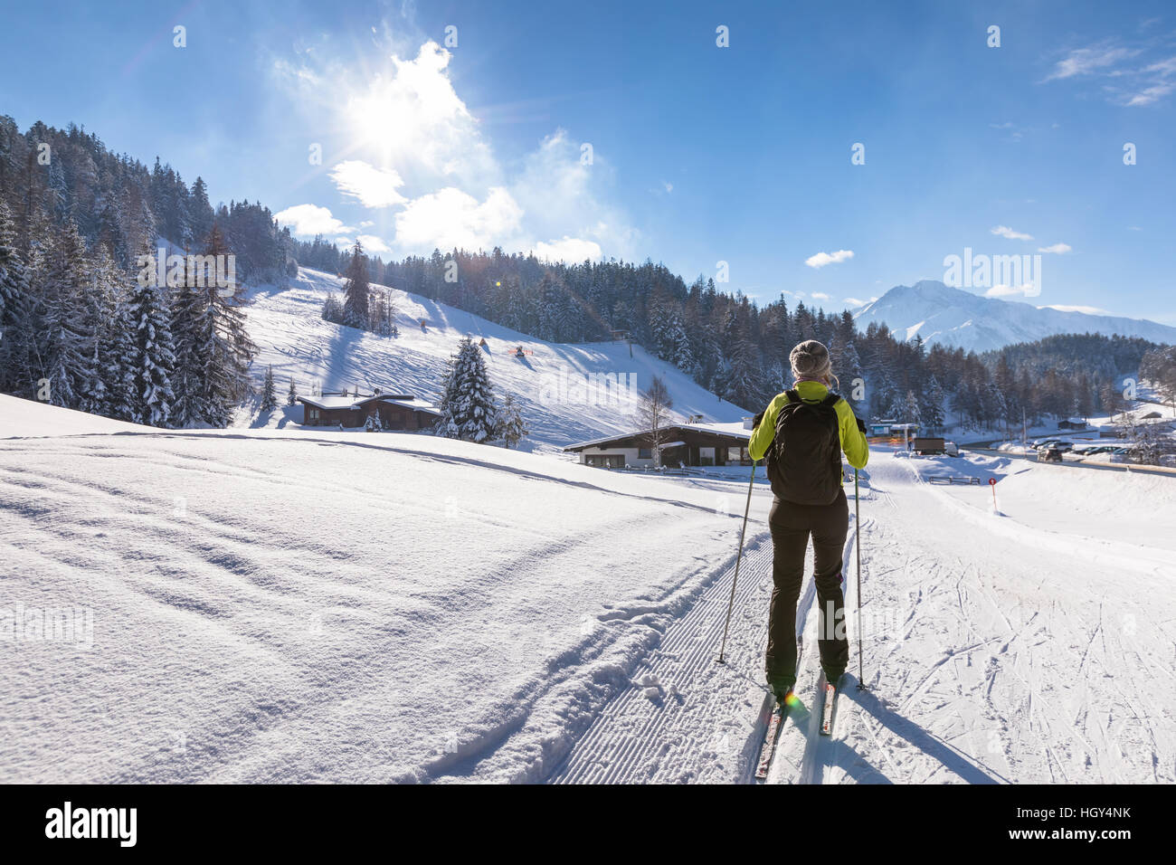 Frau macht Langlaufen auf präparierten Trail im tief verschneiten Winterlandschaft mit sonnigem Wetter und wunderschönen Bergen im Hintergrund Stockfoto