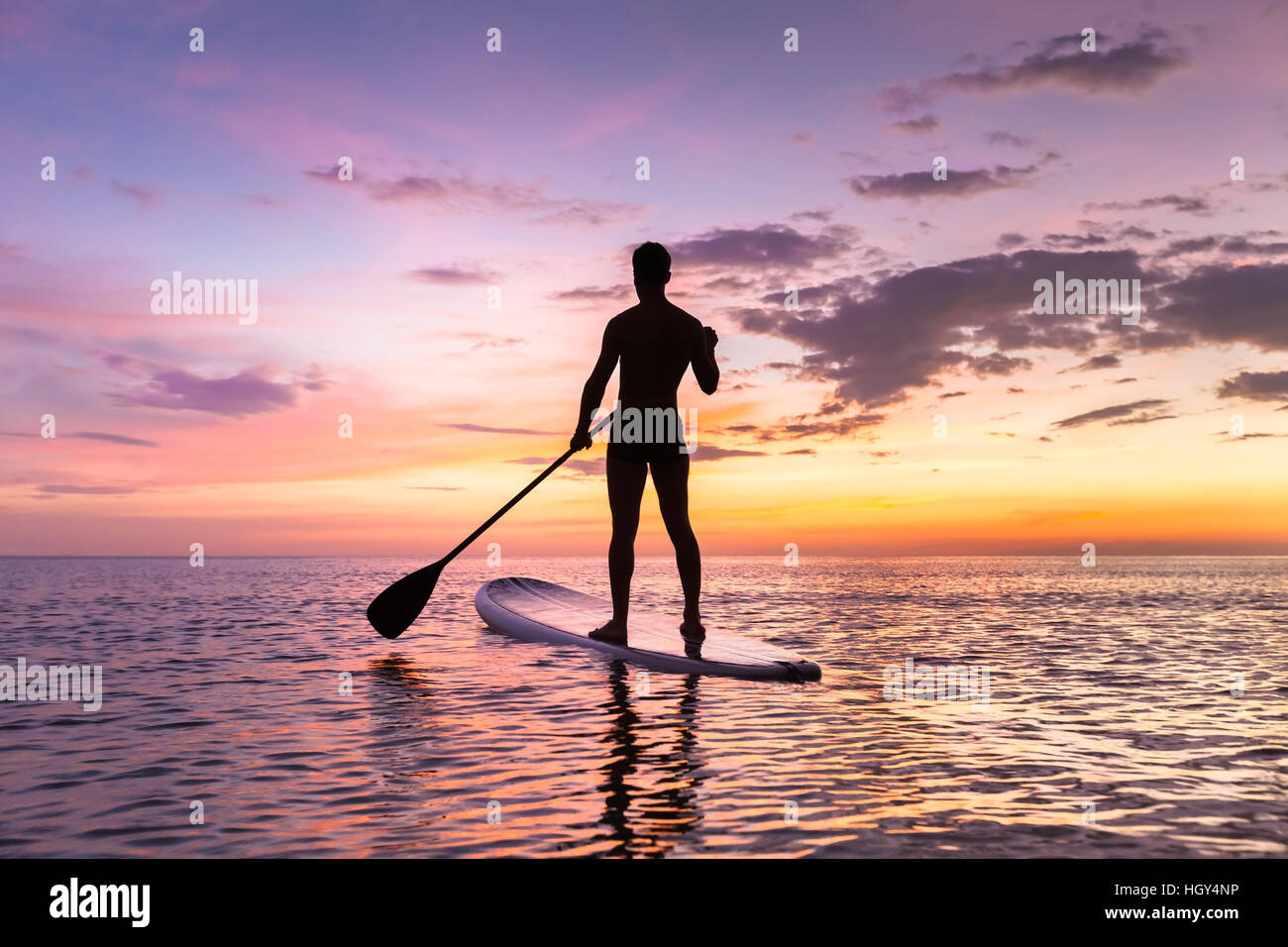 Person Stand-up-Paddle-boarding in der Abenddämmerung auf einem flachen warmen ruhigen Meer mit schönen Sonnenuntergang Farben Stockfoto