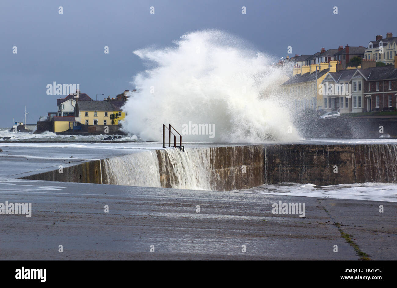 Ein Wintersturm Buffets eine Hafenmauer senden Wellen Schaum und Gischt in die Luft und Vorhänge Wasser cascading ins Meer Stockfoto