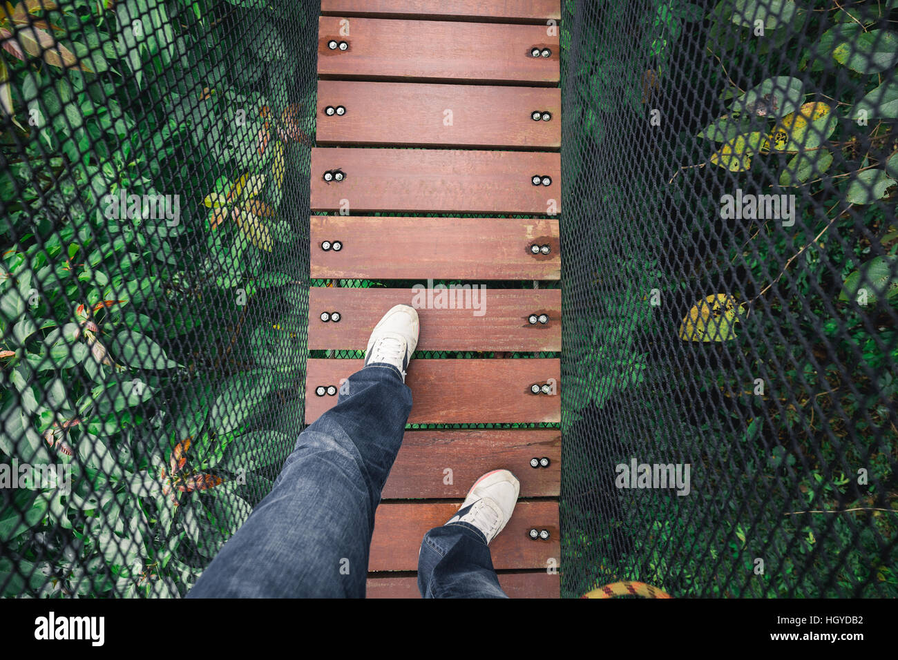 Mannes Füße und Beine auf hölzernen Brücke über die Spitze des Baumes für Sightseeing. Brücke von Black net als Wand bedeckt. Stockfoto