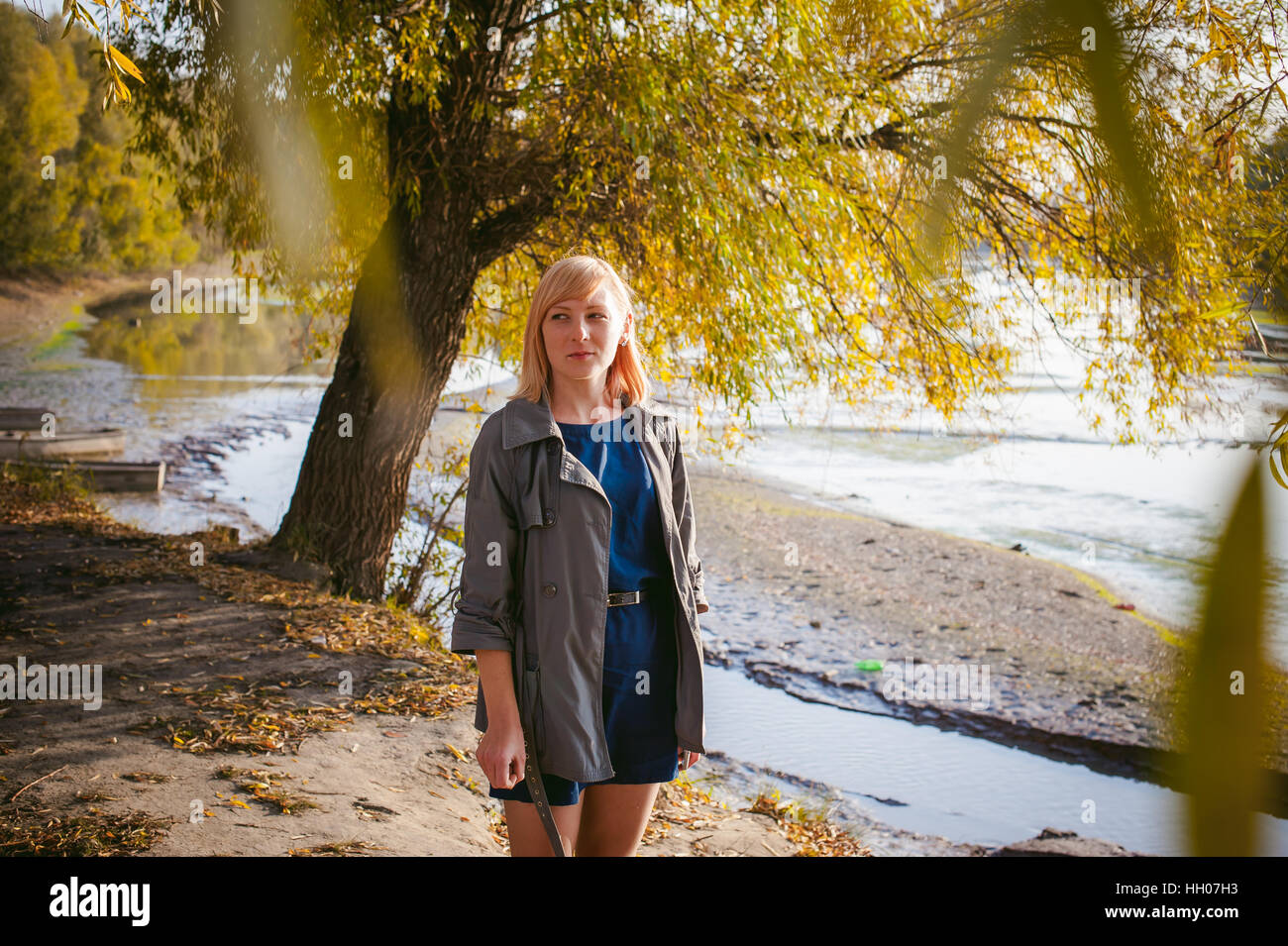 Foto ziemlich blonde Girl in Turnschuhe, Nylons und Mantel, vor dem Hintergrund der gelben Herbst Laub Stockfoto