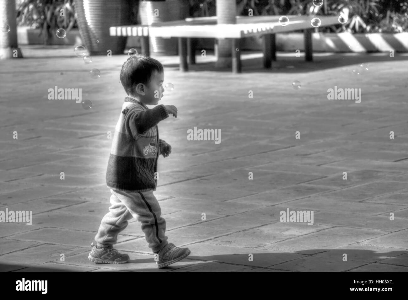 Eine asiatische Kleinkind jagen Bläschen außerhalb des Eingangs zum Fenster der Welt in Shenzhen, China. Stockfoto