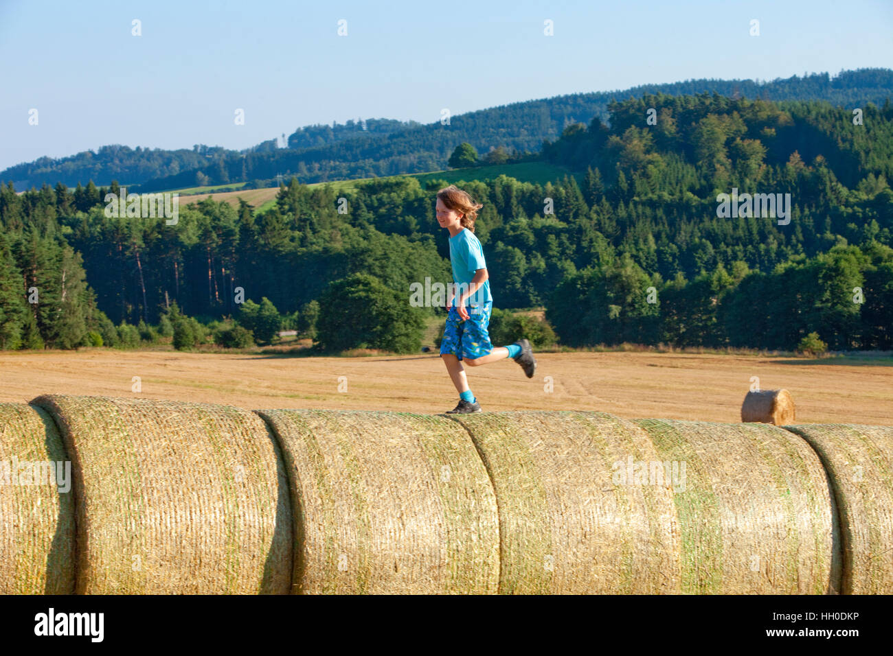 Junge läuft auf Heuballen im Sommer Stockfoto