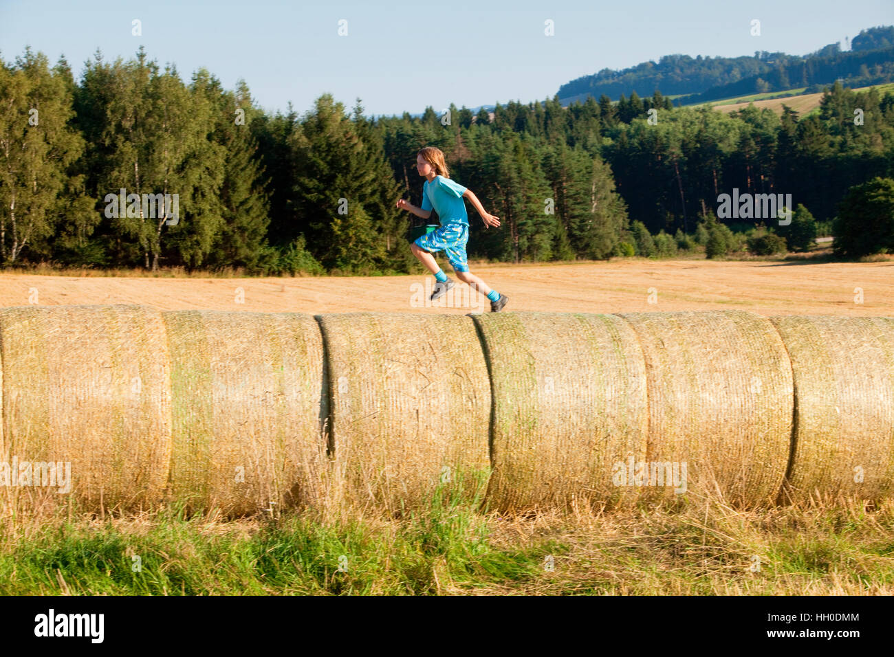 Junge läuft auf Heuballen im Sommer Stockfoto