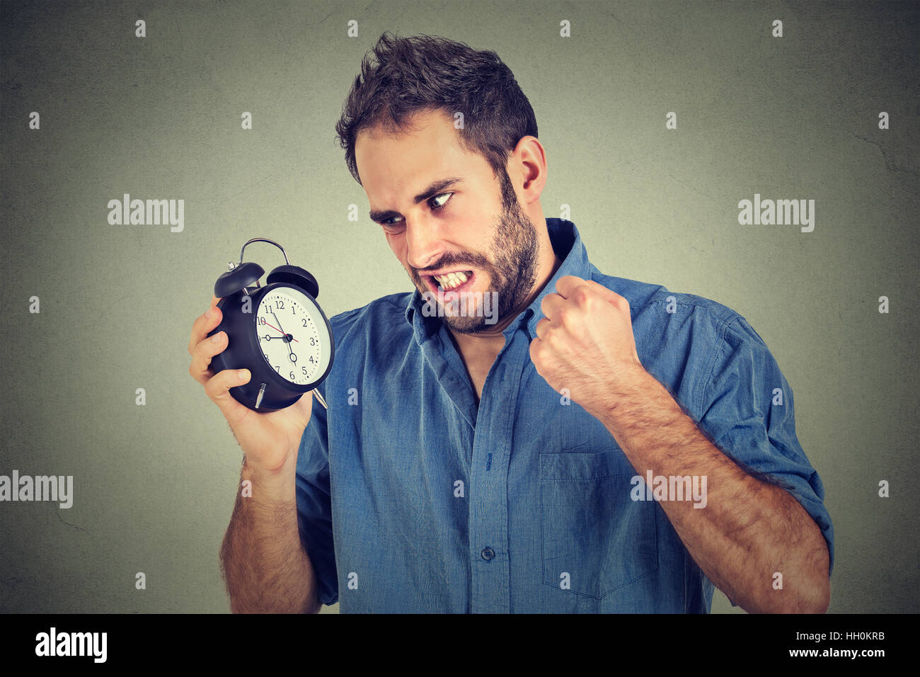 Porträt verärgert zorniger junger Mann schreiend auf Wecker auf graue Wand Hintergrund isoliert. Mitarbeiter spät dran. Zeit-Management-Konzept Stockfoto