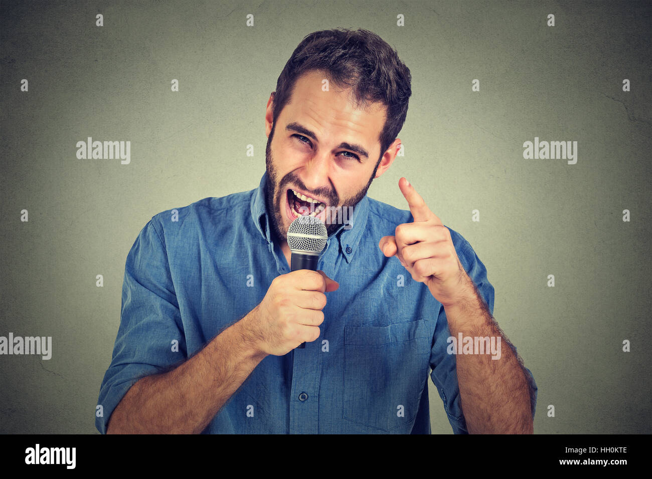 Verärgerter Mann schreien Mikrofon auf graue Wand Hintergrund isoliert. Negative Gesichtsausdrücke, Emotionen, Gefühle. Propaganda, breaking News, Kraft, s Stockfoto