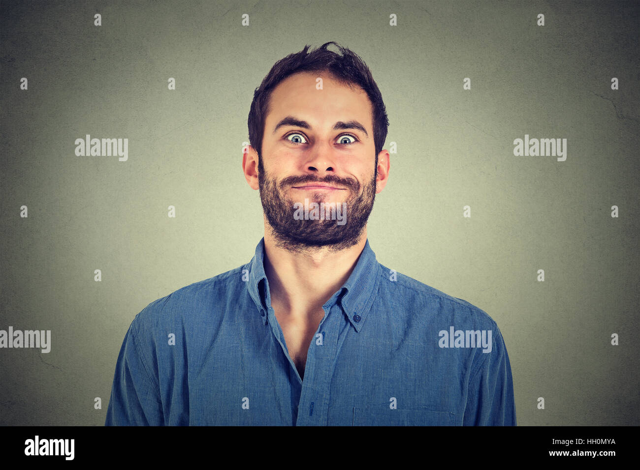 Verrückt aussehenden Mann lustige Grimassen auf graue Wand Hintergrund isoliert Stockfoto