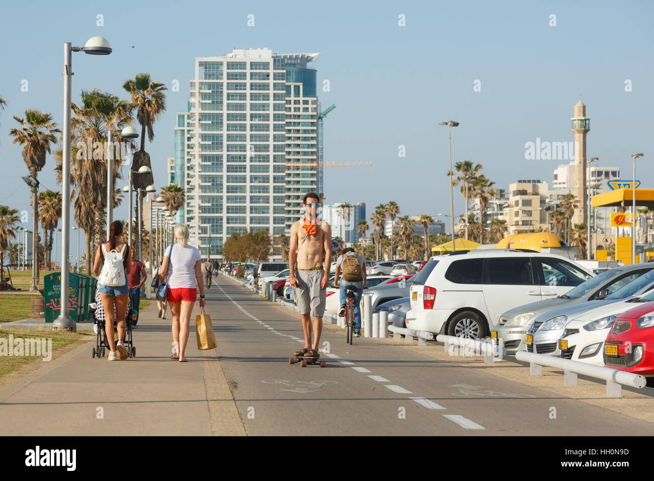 TEL AVIV, ISRAEL - 4. April 2016: Mann Ao Seepromenade ein Skateboard, Mann auf einem Fahrrad und zwei Frauen mit einem Kinderwagen am Meer in Tel Aviv, Israel auf auf Plüsch Stockfoto